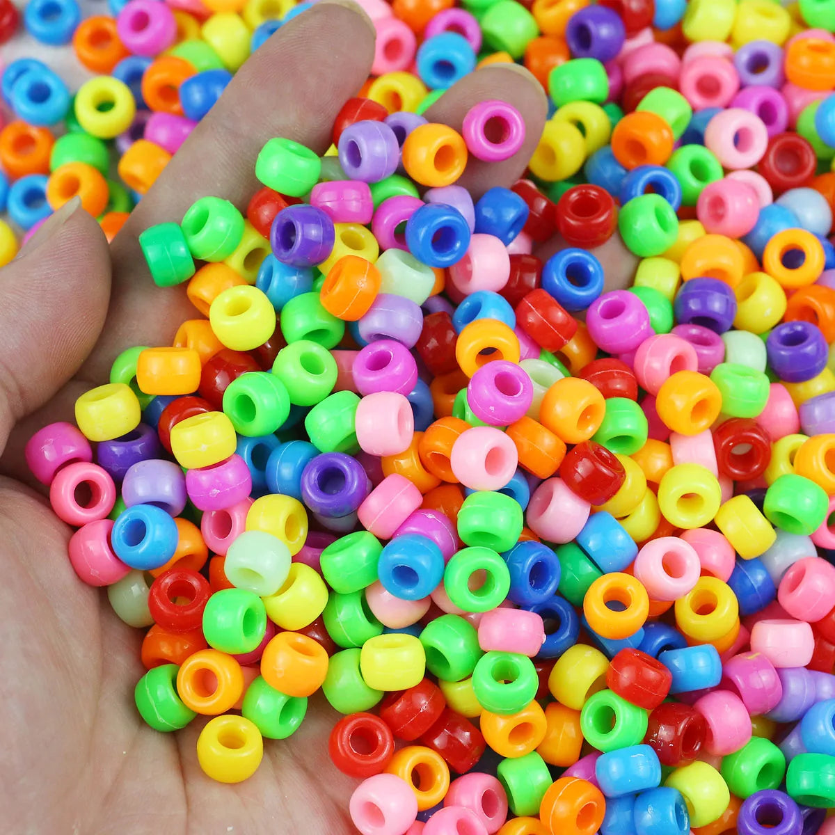 A hand holds a large pile of solid color pony beads for jewelry making and craft projects.