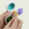 A hand holds a white suction cup spinner bath toy set with multiple colored spinners and a yellow component.