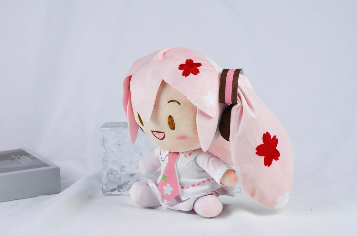 A pink Hatsune Miku plush doll with long hair and a pink outfit, sitting on a white surface.