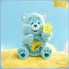 A light blue Care Bear figurine holding a yellow star, set against a bright yellow background.