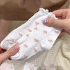 A hand is holding a white floral cotton kids sock featuring pink flowers and lace trim.