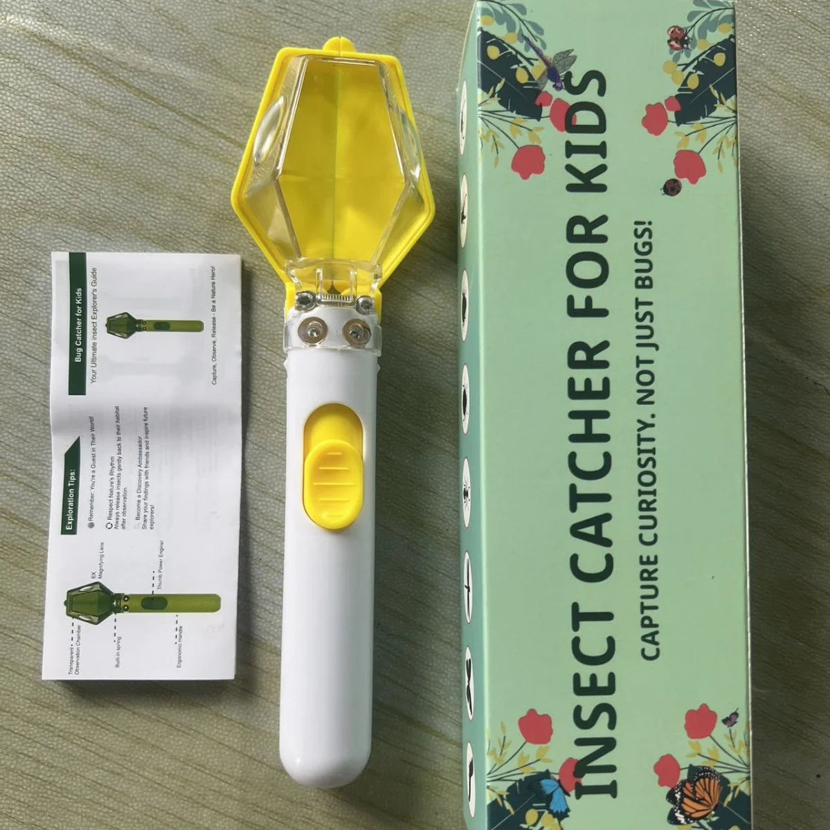 A white handheld insect catcher with a yellow magnifying lens is shown next to its packaging box.