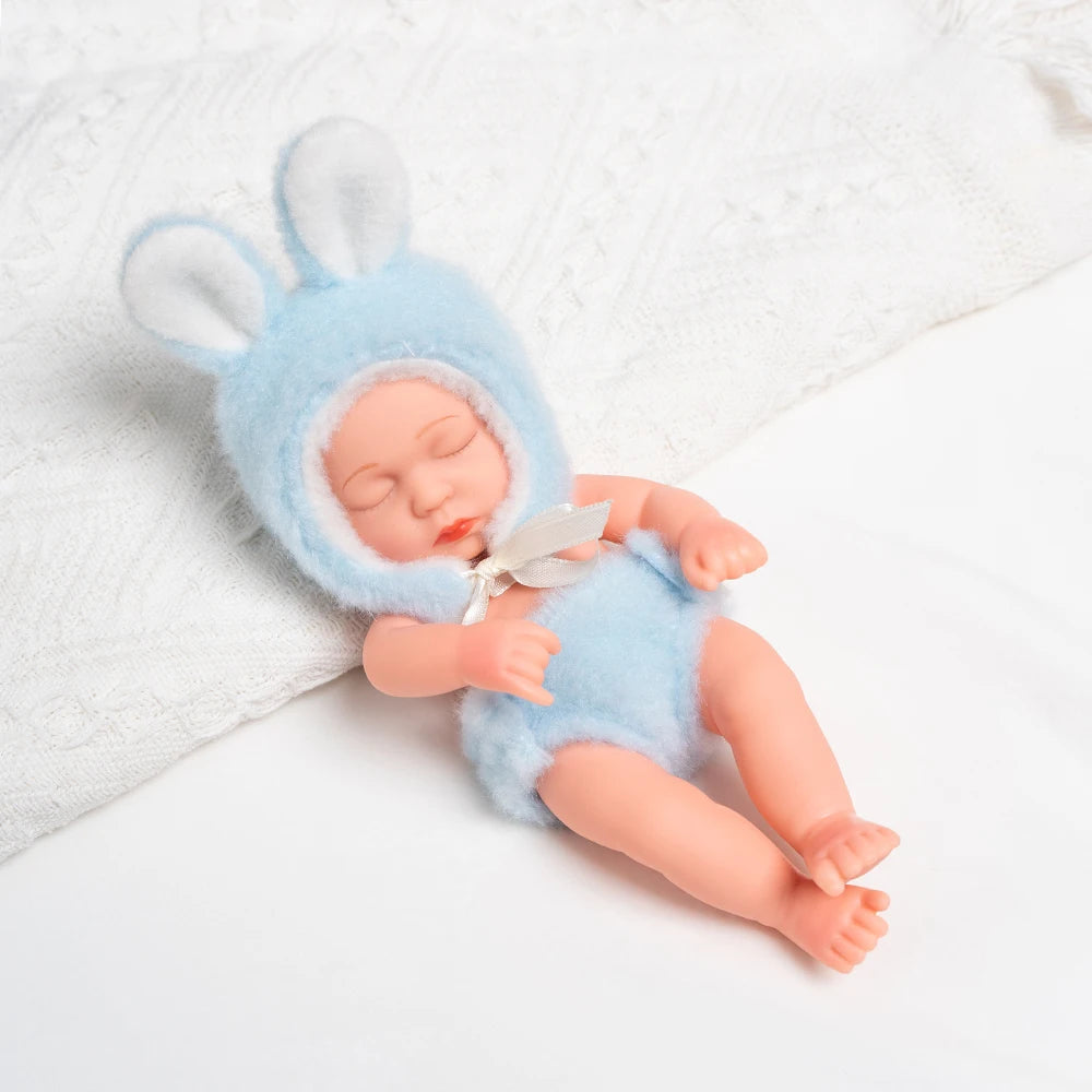 A realistic soft vinyl baby doll wearing a light blue bunny hood and matching outfit, lying on a white towel.