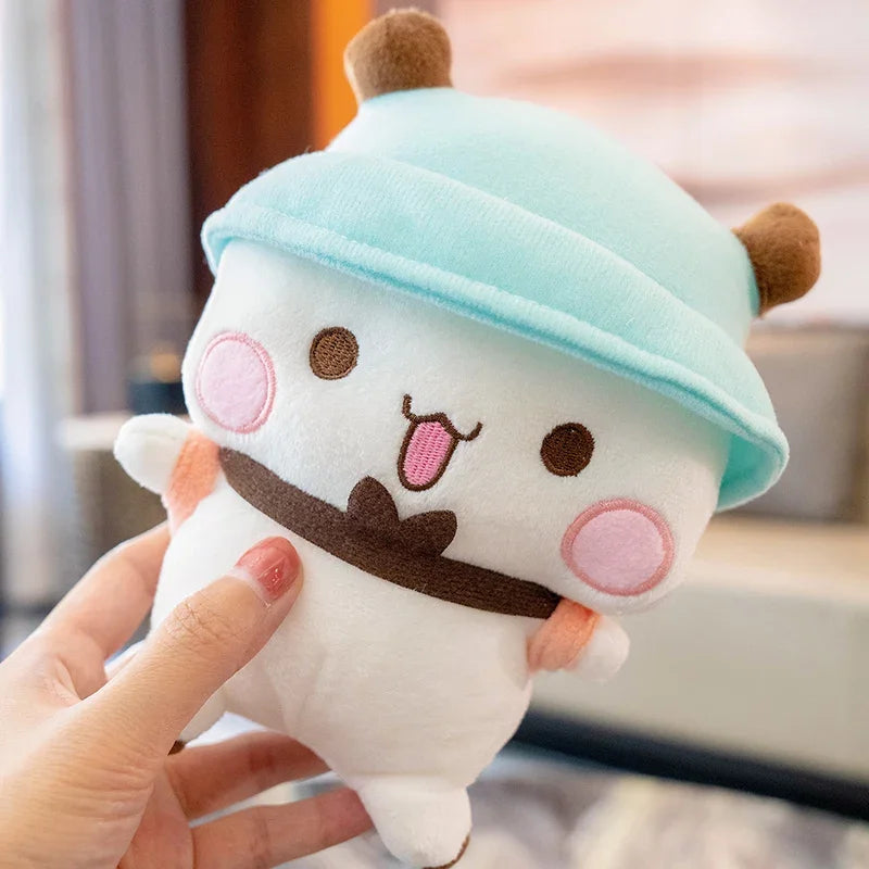 A hand is holding a white panda bear plush toy with a light blue hat and brown accents.