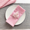 A pink linen dinner napkin set placed on a gray cloth napkin and white plate.