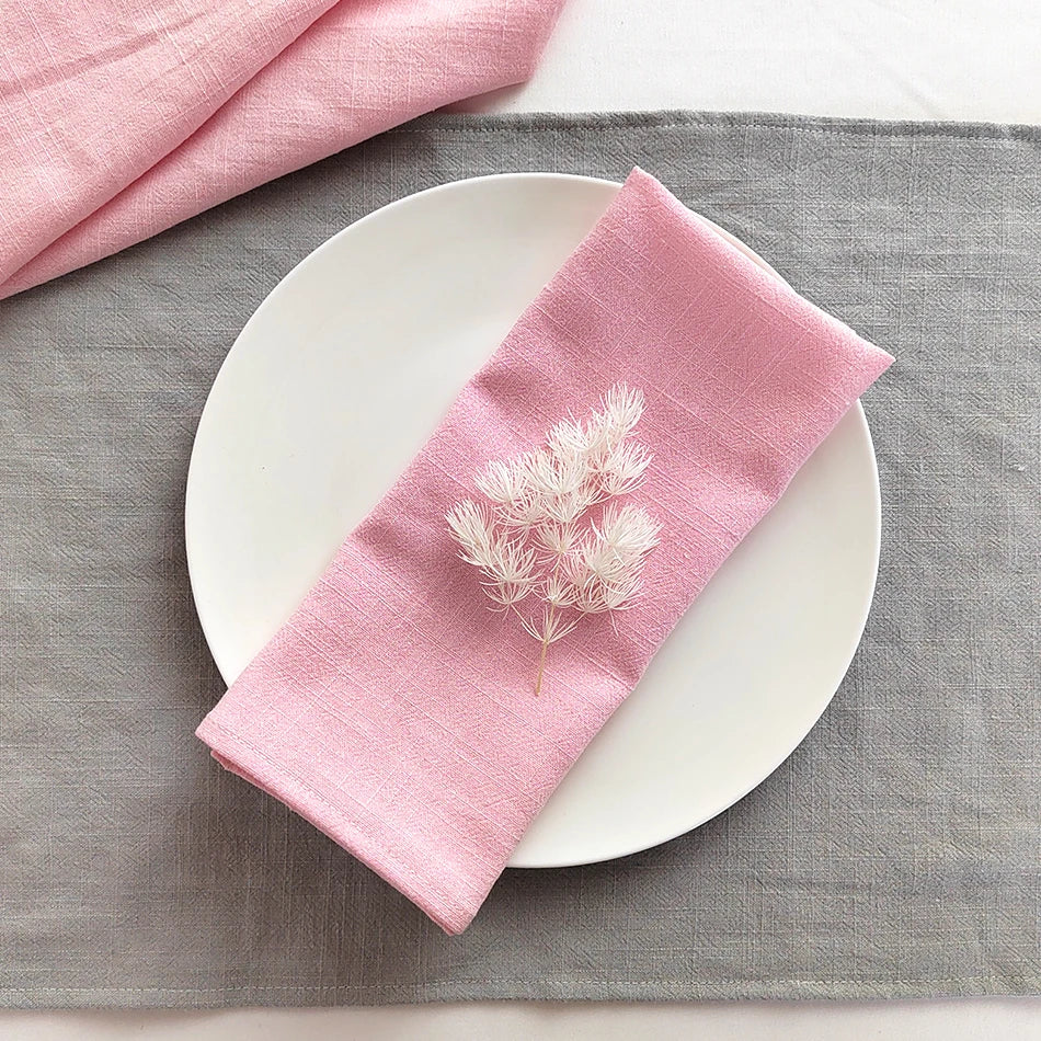 A pink linen dinner napkin set placed on a gray cloth napkin and white plate.