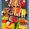 A colorful display of mini barbecue food items including sausages, meats, vegetables, and condiments for pretend play.