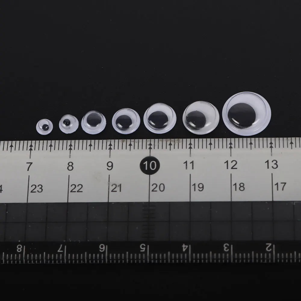 A row of clear, self-adhesive moving eyes of various sizes placed on a ruler for scale.