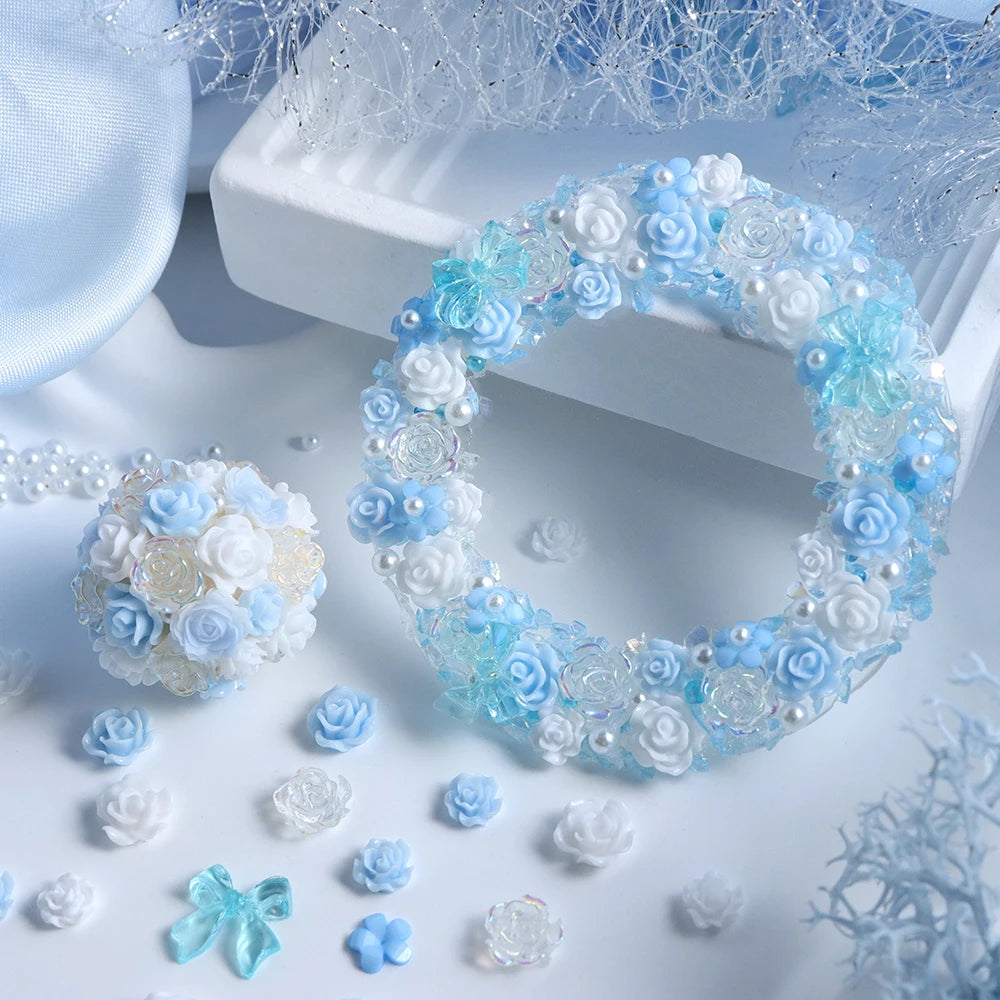 A white and blue camellia bowknot resin shaker filler wreath surrounded by small floral elements and craft supplies.