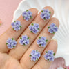 A hand displays a set of three purple resin flower ornaments on the fingers.