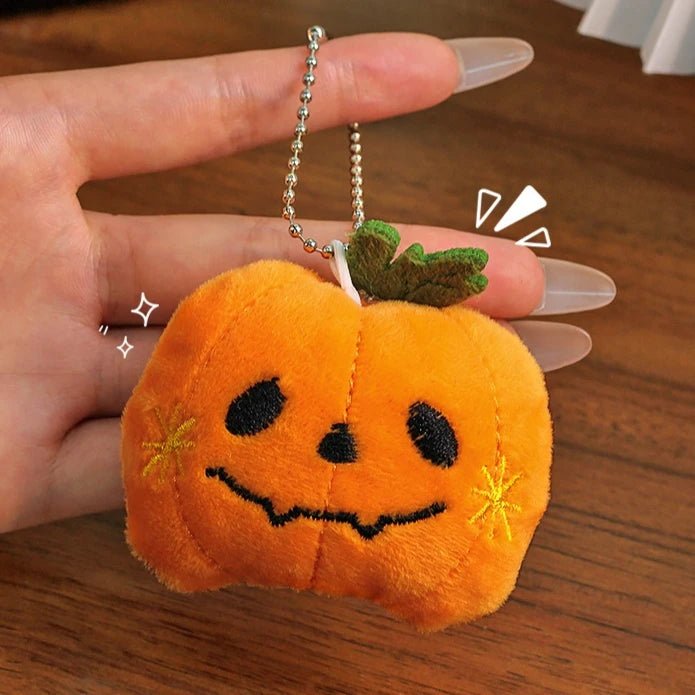 An orange pumpkin plush charm with a black carved face and green leaves, held in a hand.