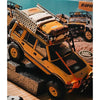 A yellow RC crawler vehicle with a roof bag and bedroll decoration set displayed on a textured surface.