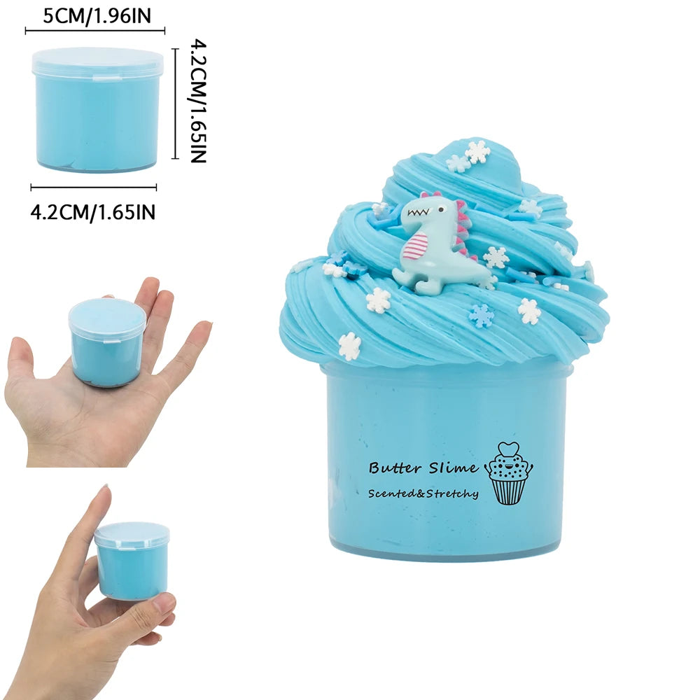A light blue butter slime kit with a dinosaur and cake design is shown in a clear container.