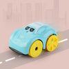 A light blue bath toy car with sunglasses is shown on a road surface against a blurred city skyline.