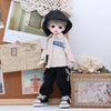 A porcelain doll dressed in a beige outfit and black hat standing next to a wooden box.