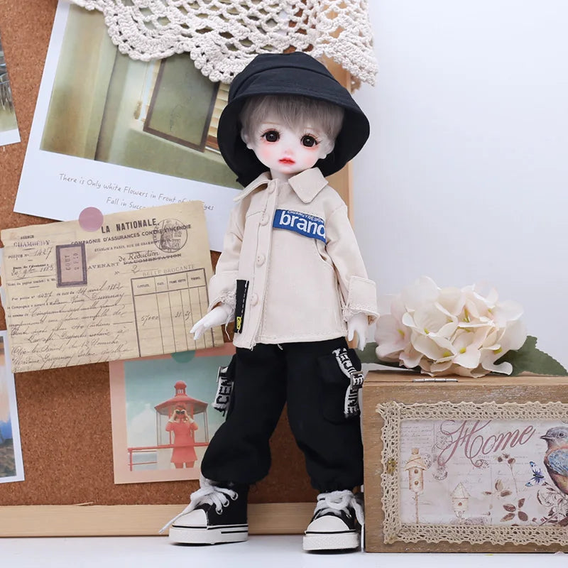 A porcelain doll dressed in a beige outfit and black hat standing next to a wooden box.