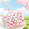 A pink and white cartoon animal keyboard keycap set is displayed on a white bag in an outdoor setting.
