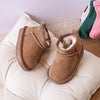 A collection of cozy winter snow boots for toddlers in various pastel colors, resting on a beige cushion.