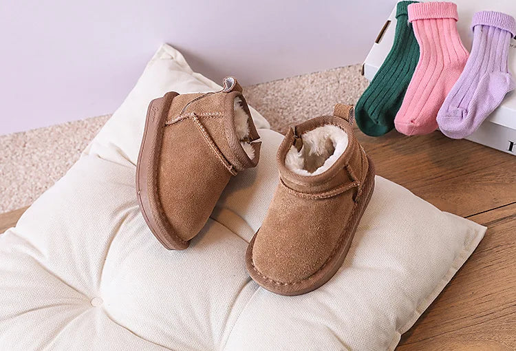 A collection of cozy winter snow boots for toddlers in various pastel colors, resting on a beige cushion.