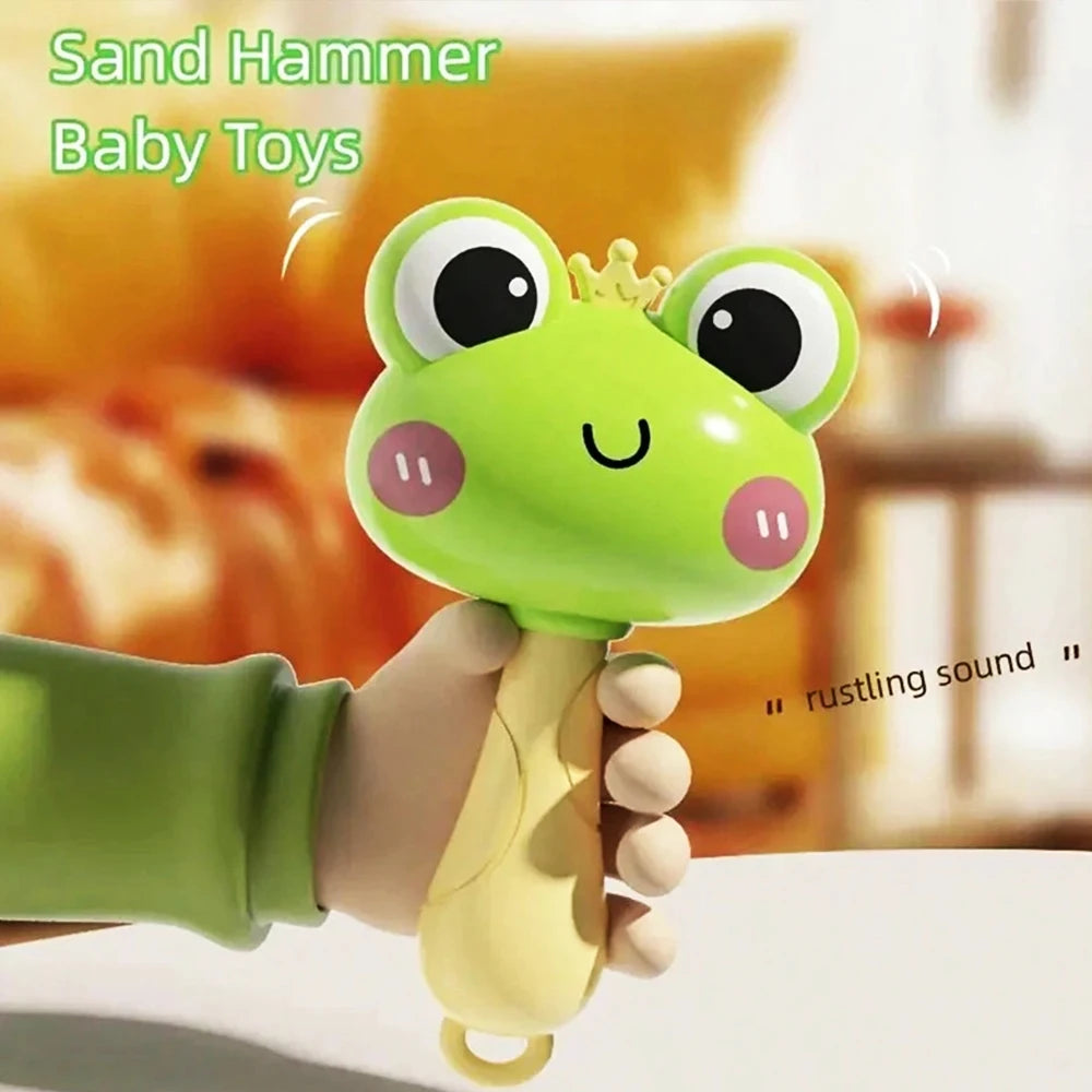A hand is holding a green sand hammer baby toy with a crown on its head