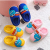 A collection of colorful cartoon dinosaur plush slippers in blue, yellow, and pink on a white fuzzy surface.