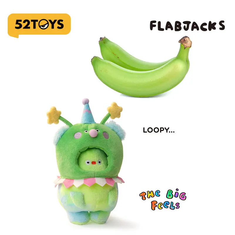 A green banana plush pendant charm with a face and pink accents is shown next to a whole green banana.