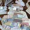 A collection of vintage washi paper sticker sheets in various grid and striped patterns scattered on a wooden surface.