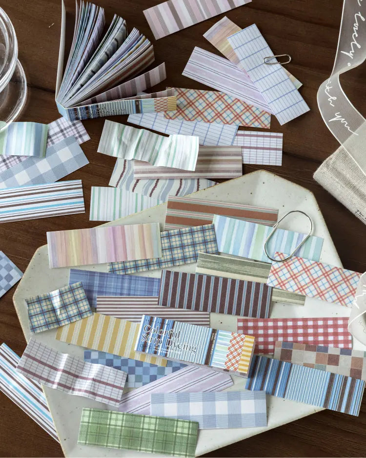 A collection of vintage washi paper sticker sheets in various grid and striped patterns scattered on a wooden surface.