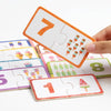 A hand holds a wooden number matching puzzle piece showing the number 7, with other pieces visible.