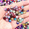 A hand holds a collection of round glass crackle beads in various colors and shades for jewelry making.