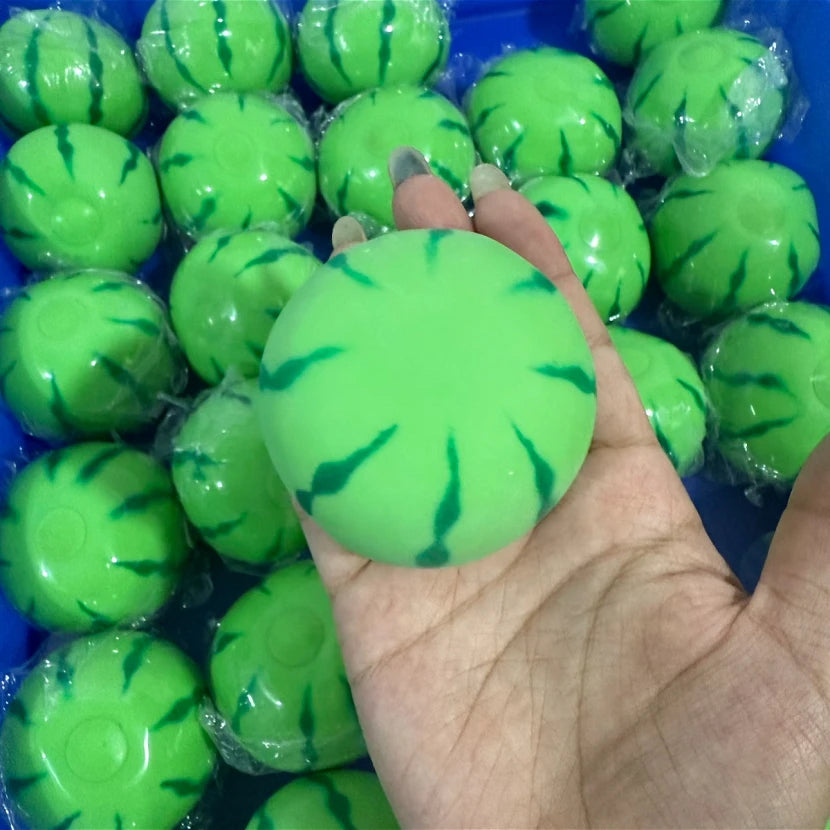 A hand holds a bright green watermelon squishy stress ball with a textured surface, surrounded by other similar squishies.