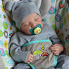 A sleeping baby doll wearing a gray knitted hat and a matching outfit with fruit and vegetable designs.