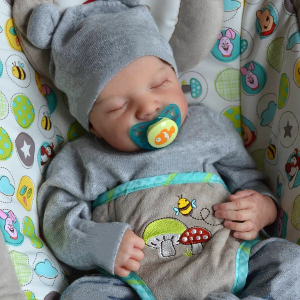 A sleeping baby doll wearing a gray knitted hat and a matching outfit with fruit and vegetable designs.