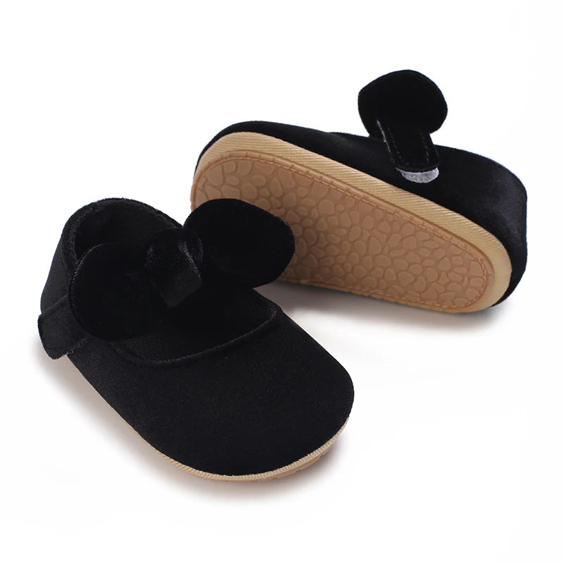 Black lace-trimmed baby girl moccasin shoes with a bow shown from the side.