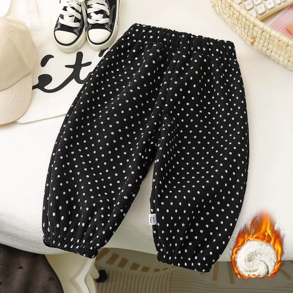 Black fleece-lined polka dot pants with white spots laid out on a white surface.