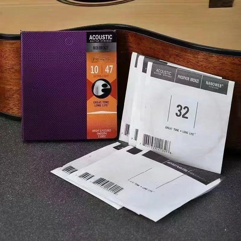A box of Acoustic Guitar Strings with a purple label and several white string packages is displayed on a dark surface.