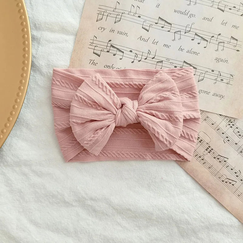 A pink knitted fabric headband with a large bow rests on a sheet of sheet music.