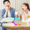 A young man and woman are using a Bluetooth karaoke speaker system with wireless microphones in a bright indoor setting.