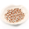 A pile of small, round, rose gold spacer beads resting on a white dish.