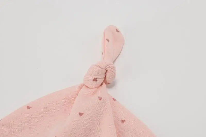 A pink knitted baby hat with a bow detail and small heart patterns.