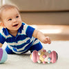 A baby is playing with a pink and yellow Montessori crawling roller toy on a light surface.