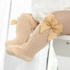 A pair of beige lace knee socks for a baby girl with a decorative bow.