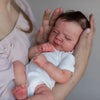 A newborn baby with hand-rooted hair is being held by a person's hands.