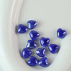 A collection of small, shiny blue heart-shaped ceramic beads arranged on a white surface.