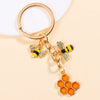Gold-toned enamel flower keychain featuring a bee and an orange honeycomb shape.