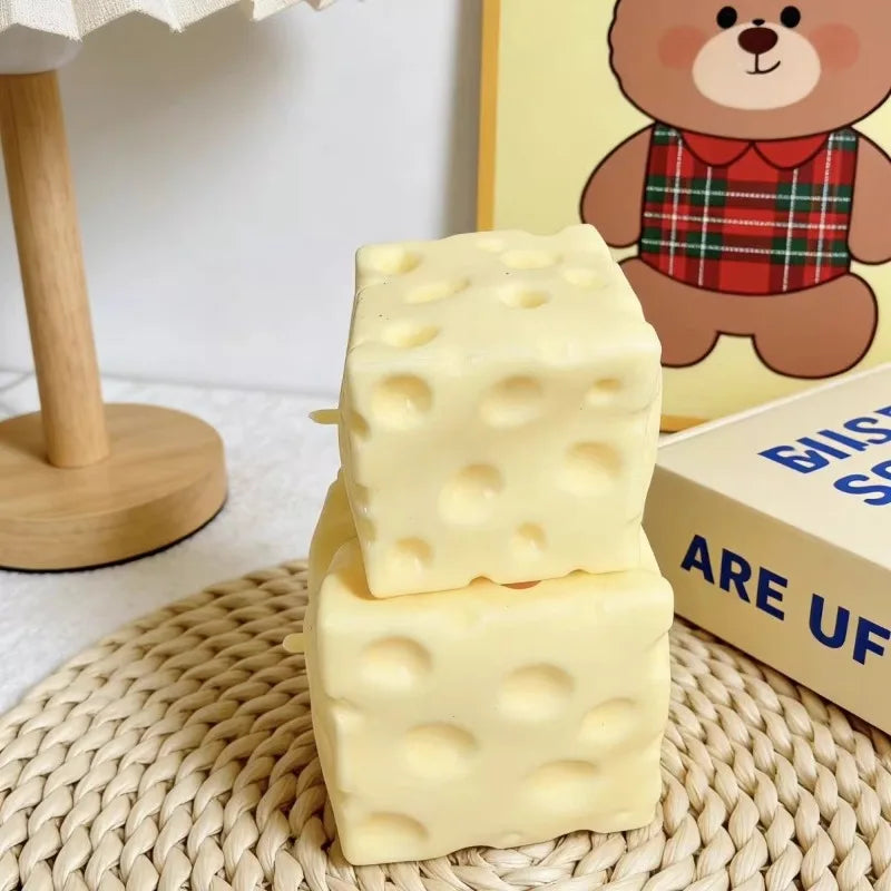 A stack of yellow cheese cubes, a deformable sensory fidget toy, rests on a woven mat next to a teddy bear illustration.
