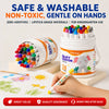 A hand holds a white container of colorful twist-up crayons, with a pile of crayons visible next to it.