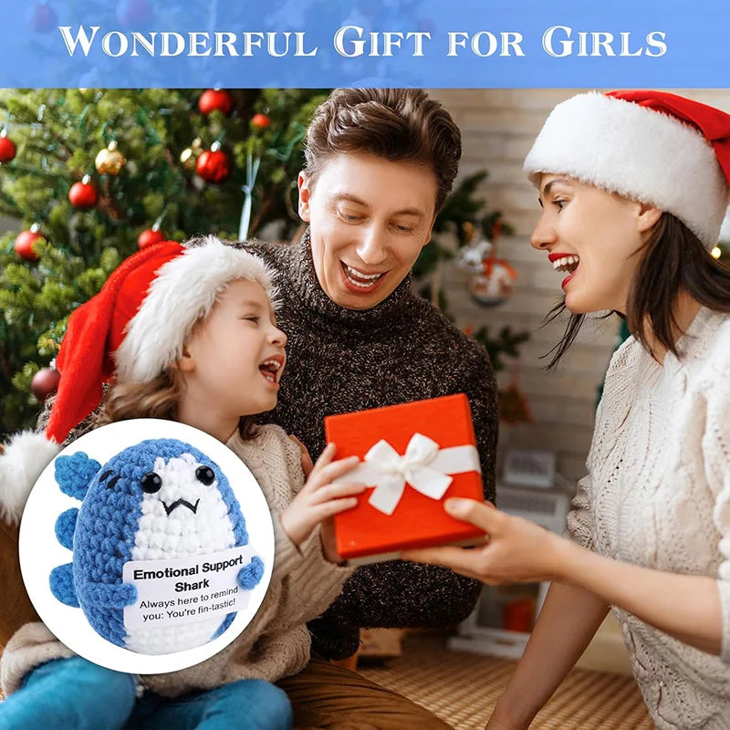 A girl is receiving a red gift box from an adult, with an emotional support shark plush visible.