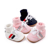 A set of pink and navy ankle-hugging baby booties with white laces and anti-slip soles.