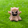 A light beige cartoon pumpkin bear figurine with a menacing black face carved into it, resting on green grass.